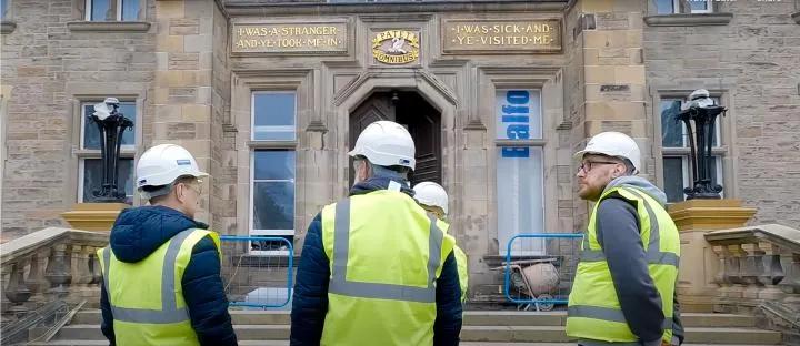 Group in high vis jackets entering building "I was a stranger and ye took me in" over the threshold.