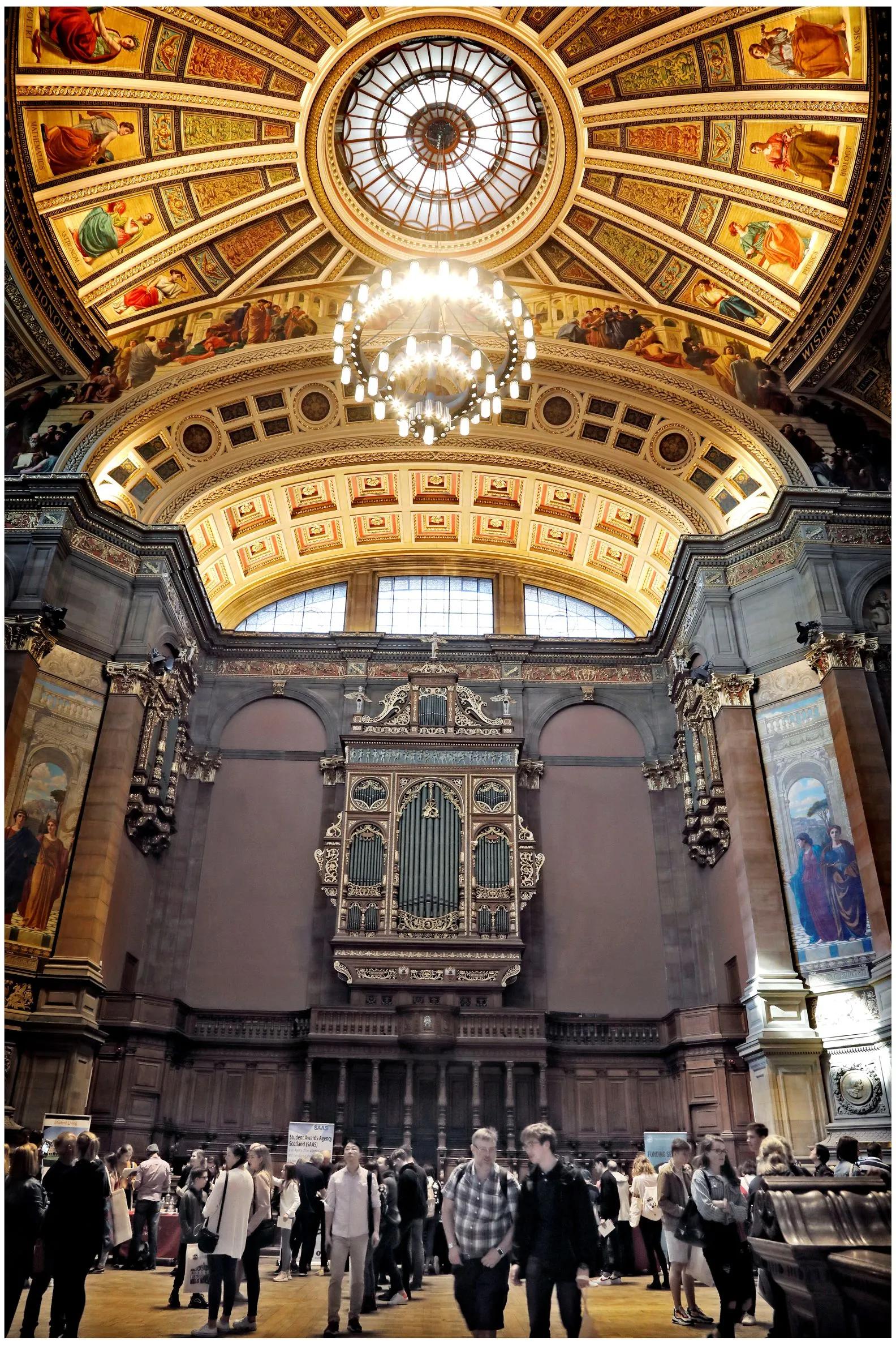 Visitors walk about under the ornate ceiling frescos of McEwan Hall
